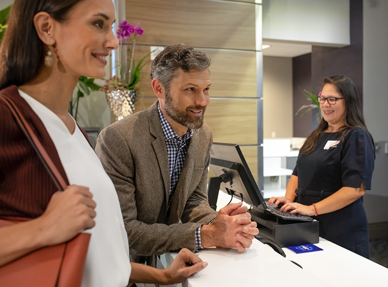 A smiling man and woman have a conversation with a front desk agent at a Club Wyndham resort.