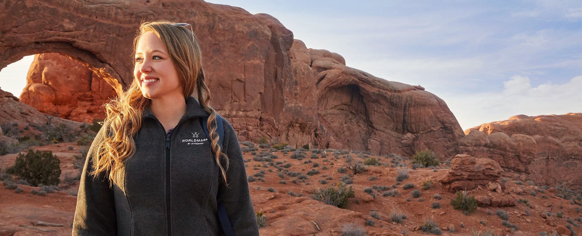 A woman wearing a WorldMark by Wyndham zip-up jacket is at Arches National Park in Moab, Utah.